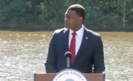 EPA administrator stands at an outdoor podium with water flowing in the background