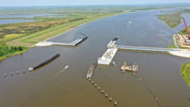 Photo shows aerial view of a lock on the water with land covered in green grass on either side