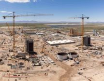 Construction site photo includes two cranes and structures in progress. Mountains are visible in the skyline in the background. 